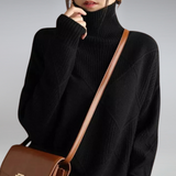 Person wearing a black turtleneck sweater with a brown shoulder bag on a gray background