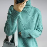 Person wearing a teal sweater holding a camera against a plain background