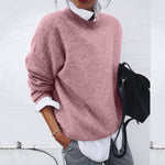 Person wearing a pink sweater with a white shirt and gray pants, holding a black bag against a white background.
