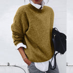 Person wearing a mustard yellow sweater with a white shirt and gray pants, holding a black backpack against a white background.