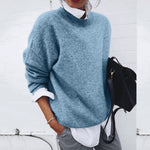 Person wearing a blue sweater with a white shirt and gray pants, holding a black backpack against a white background.